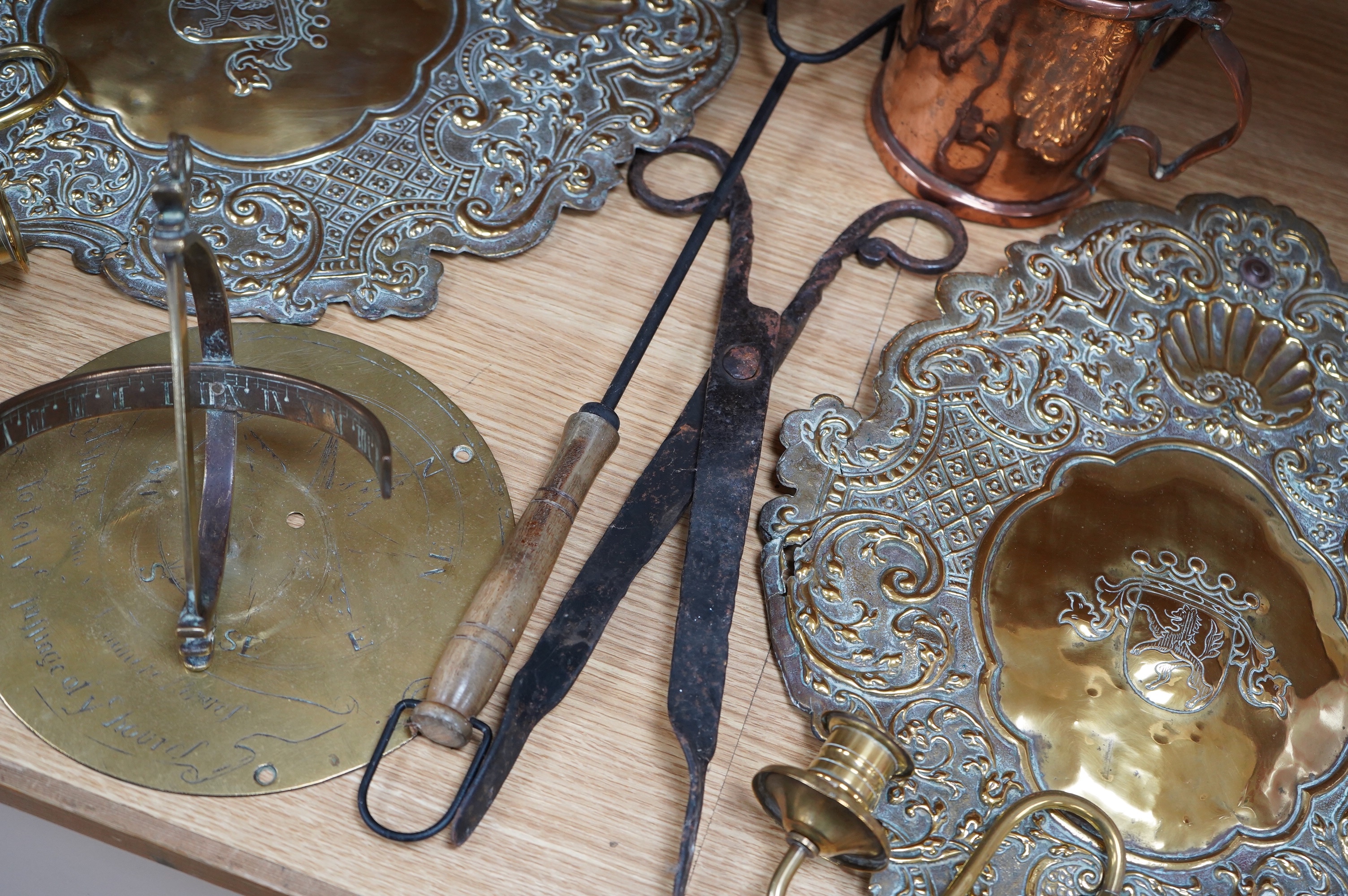 A pair of brass repousse wall sconces, a copper two handle mug, a small brass sun dial, a pair of tongs and a roasting trivet. Condition - poor to fair